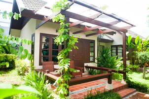 Una casa con porche, sillas de madera y una planta en maceta.