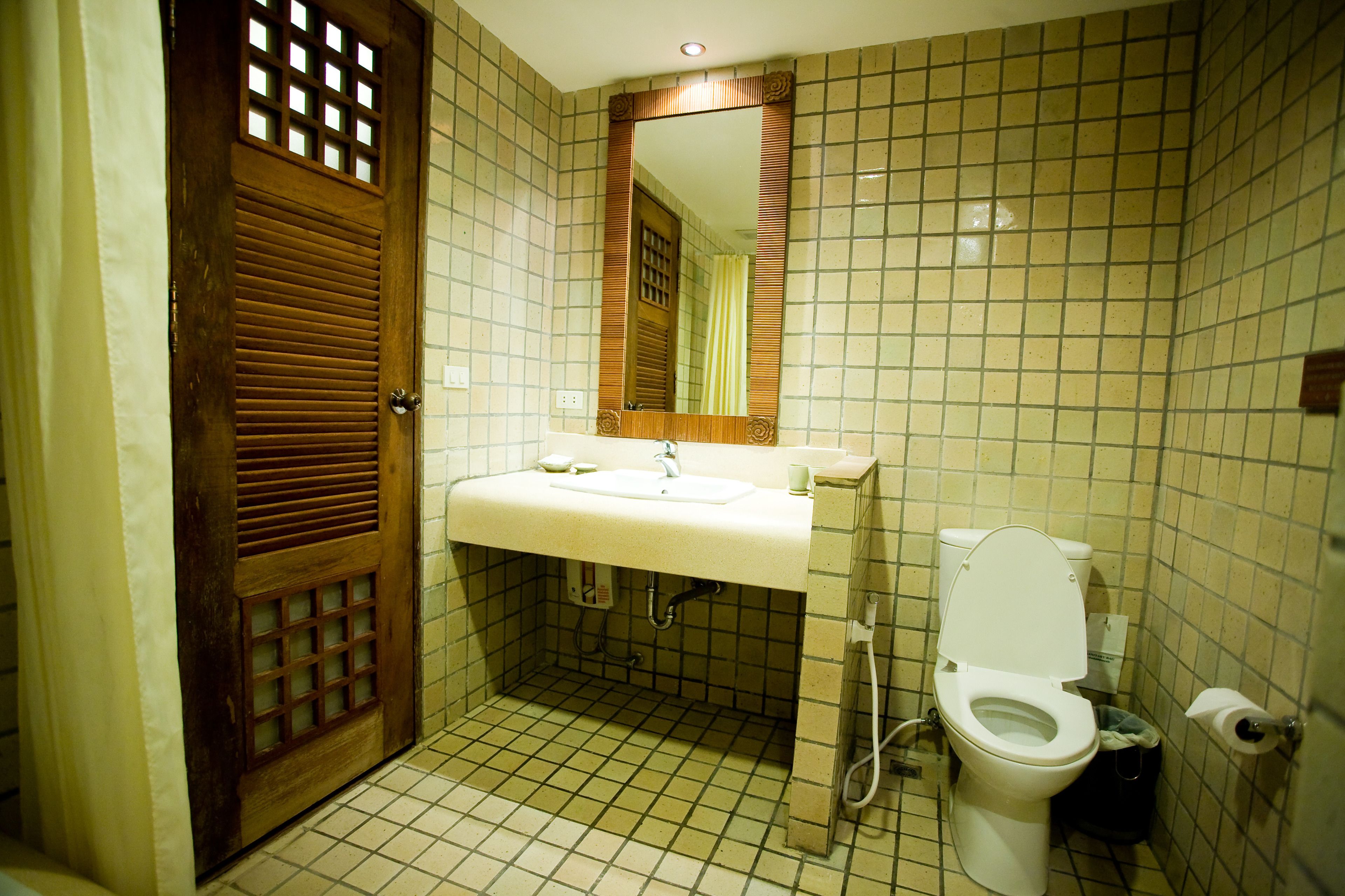 A bathroom with a wooden door, a sink, a mirror, and a toilet.