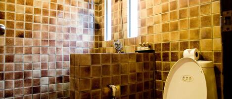 A bathroom with a tiled floor and walls, a toilet, a shower, and a window.