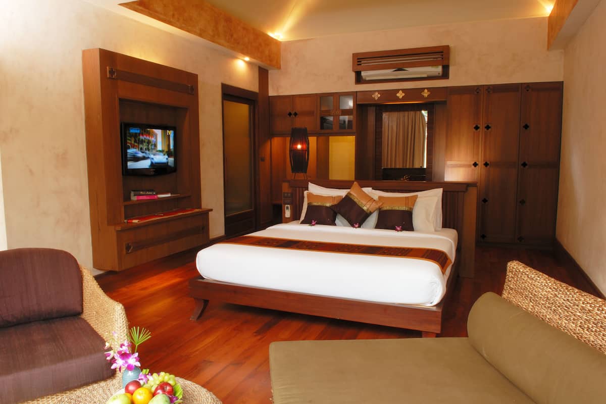 Quarto de hotel com uma cama grande, televisão, móveis de madeira e uma cesta de frutas.
