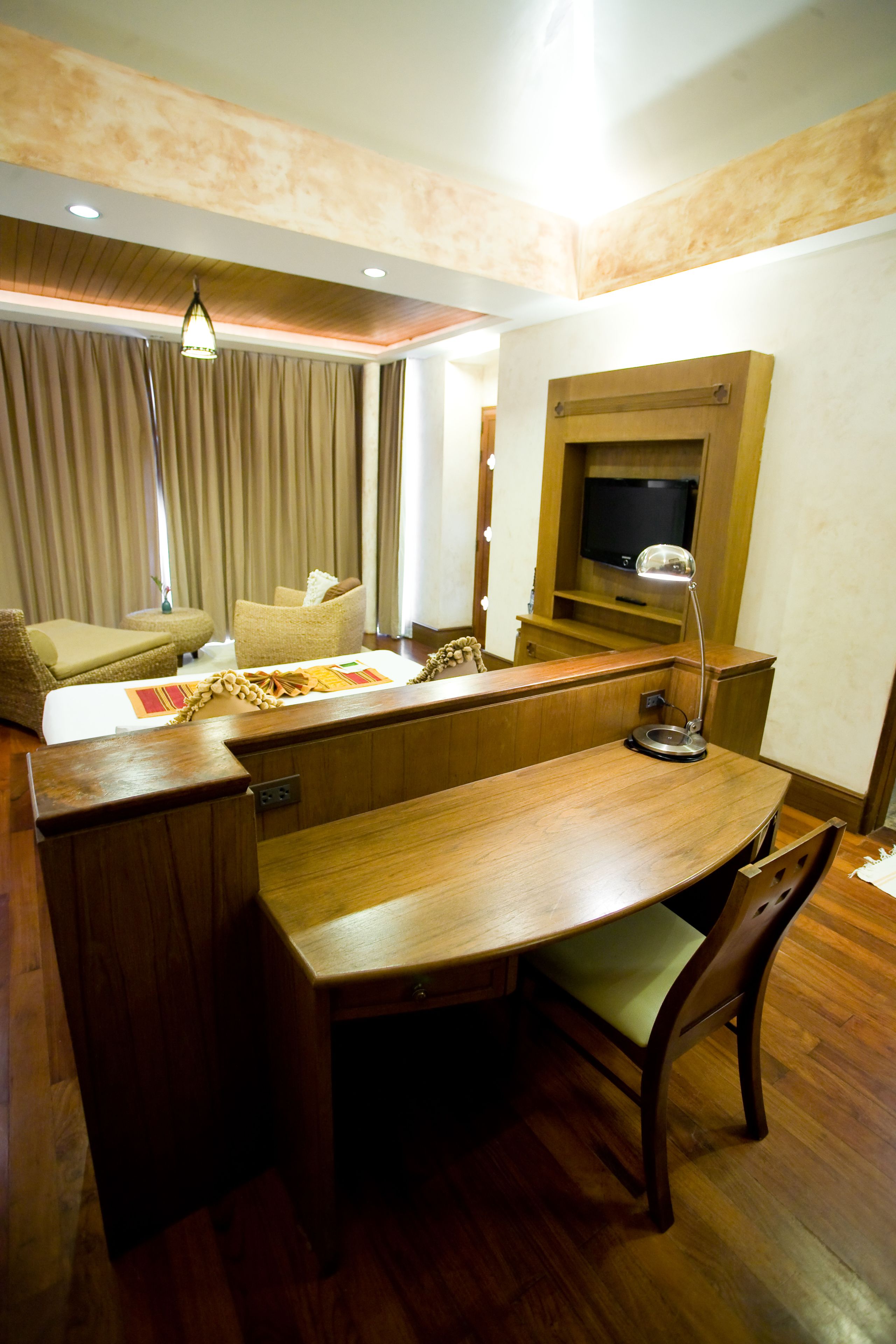 A hotel room with a wooden desk, a television, a lamp, and a sofa.