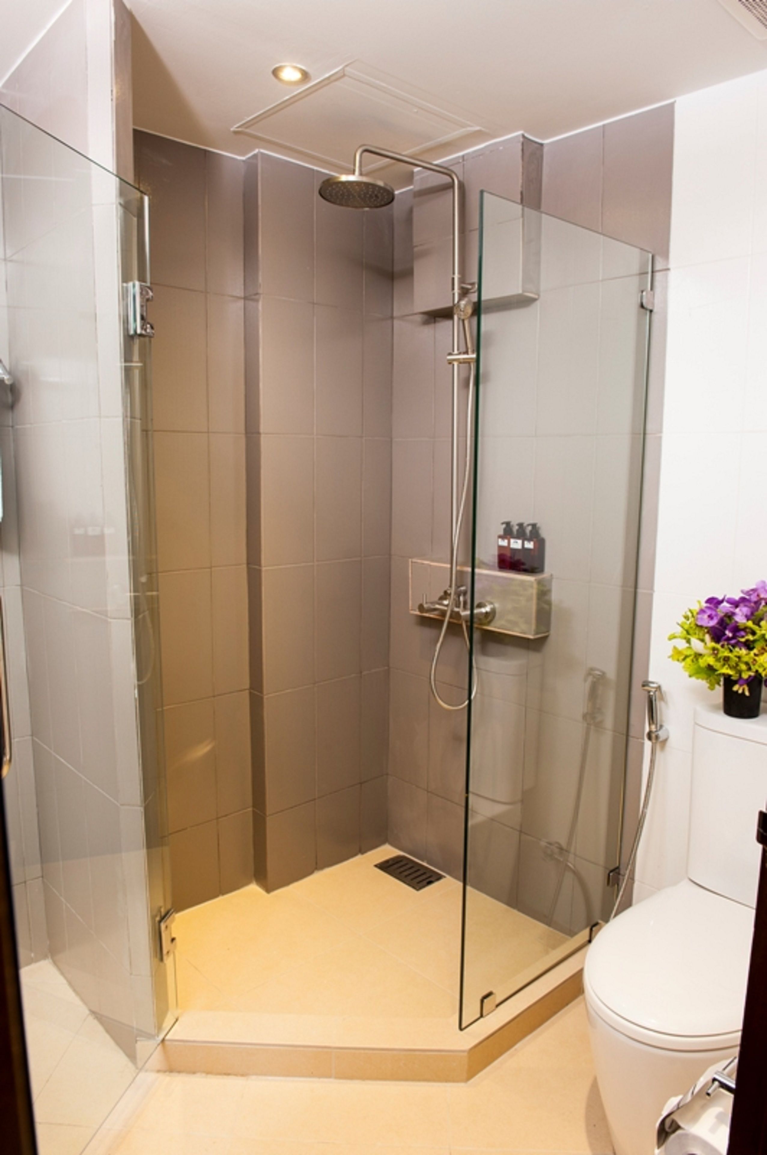 A glass-enclosed shower stall with a handheld showerhead, a glass door, and a small shelf with toiletries.
