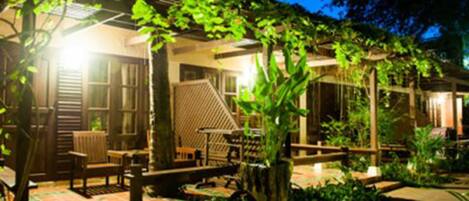 A cozy outdoor seating area with wooden furniture and a pergola, surrounded by lush greenery.