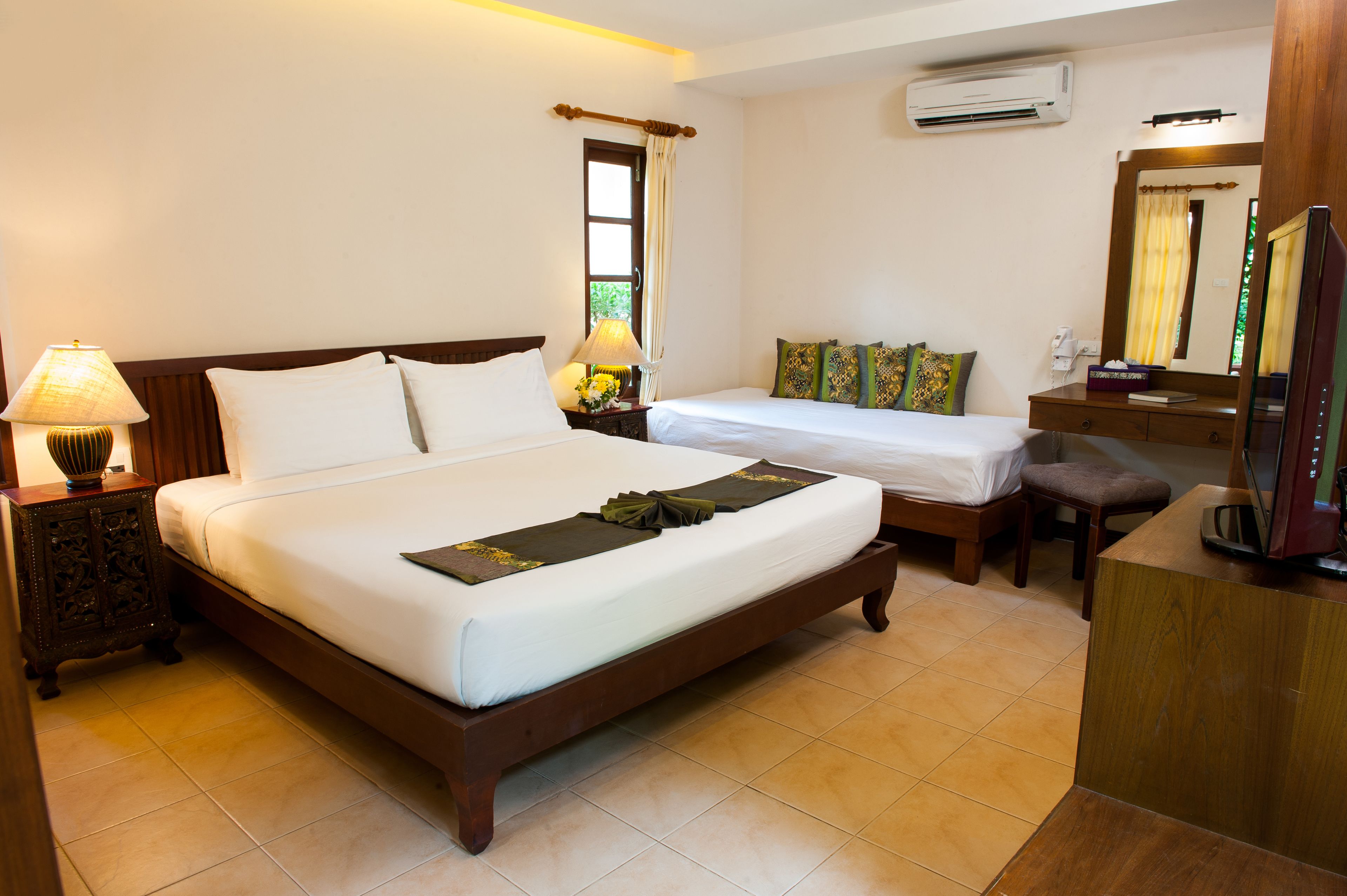Una habitación de hotel con una cama grande, una cama más pequeña, un escritorio, un espejo y un equipo de aire acondicionado.