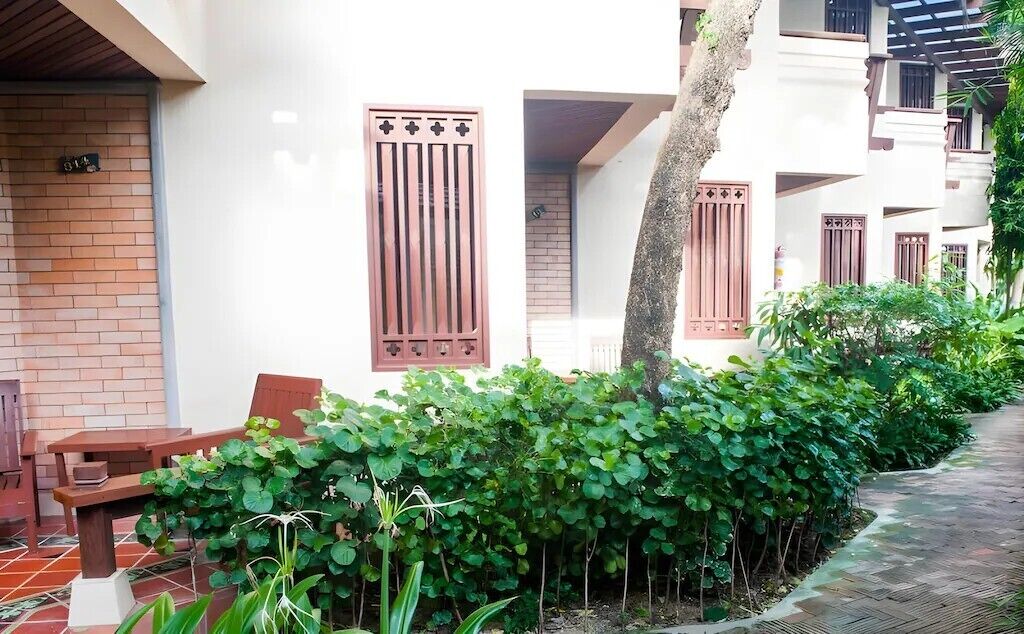 A courtyard with a brick wall, a wooden bench, and a row of green plants.