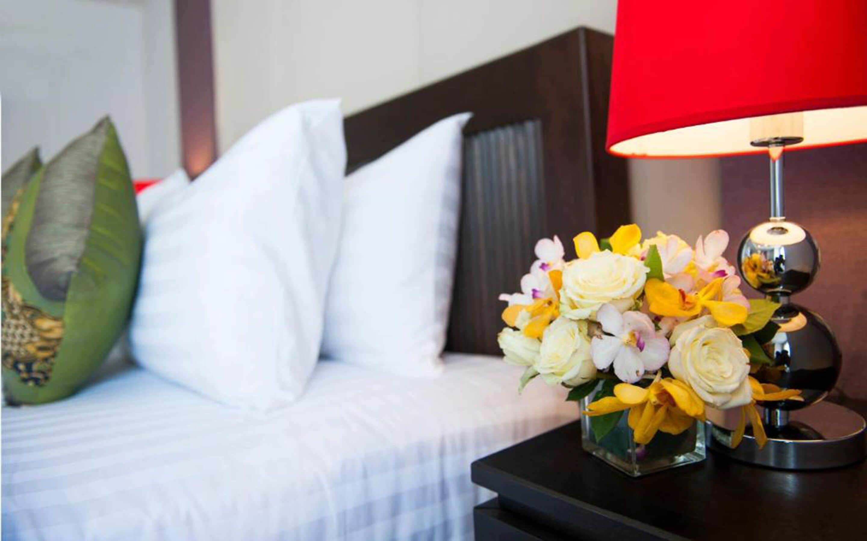 A neatly made bed with white pillows and a red lamp beside it.