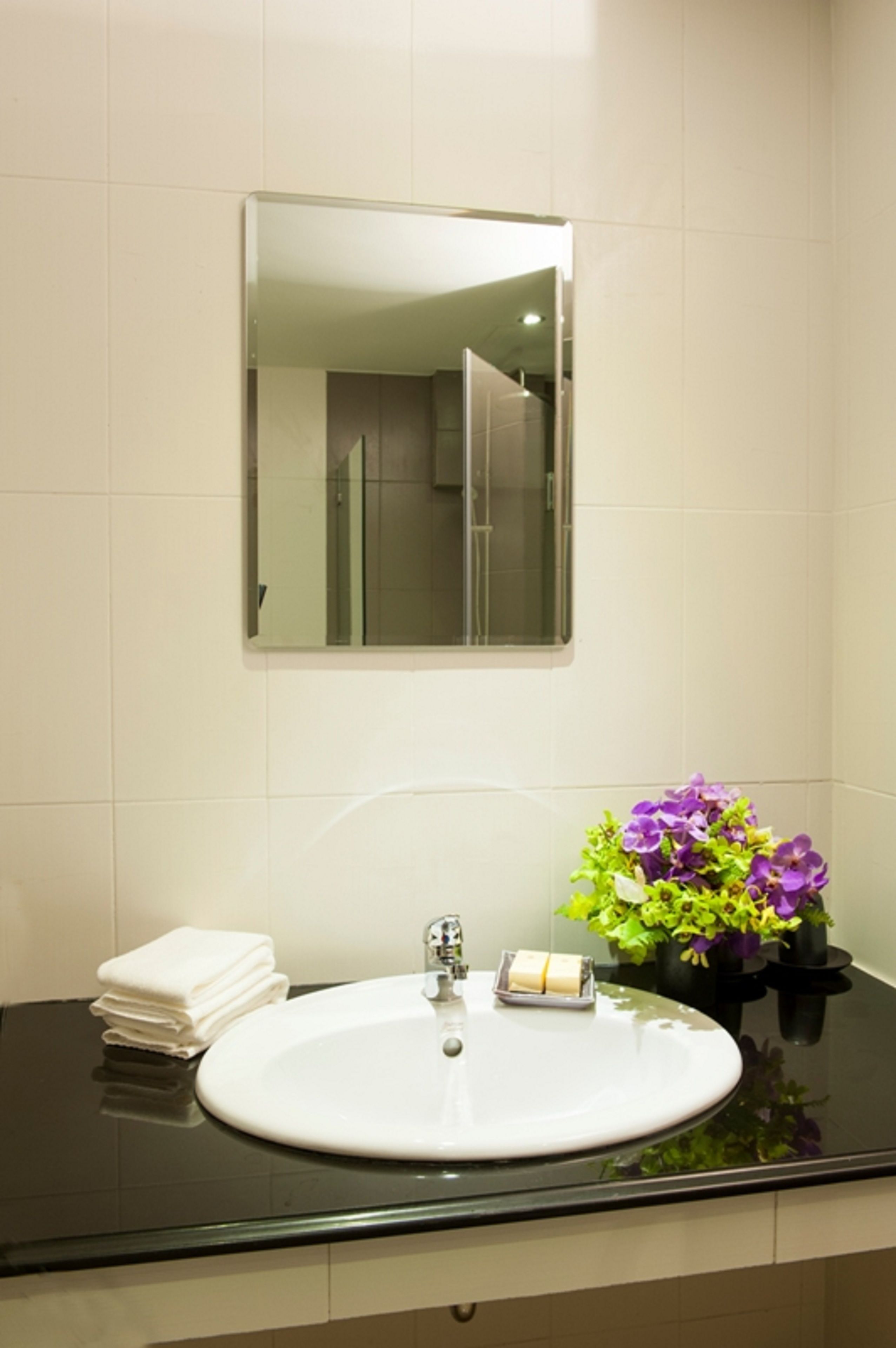 A bathroom with a white sink, a mirror, and a stack of white towels.