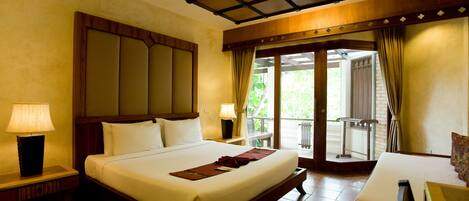 A hotel room with a large bed, two bedside lamps, a wooden headboard, and a balcony with a view of greenery.