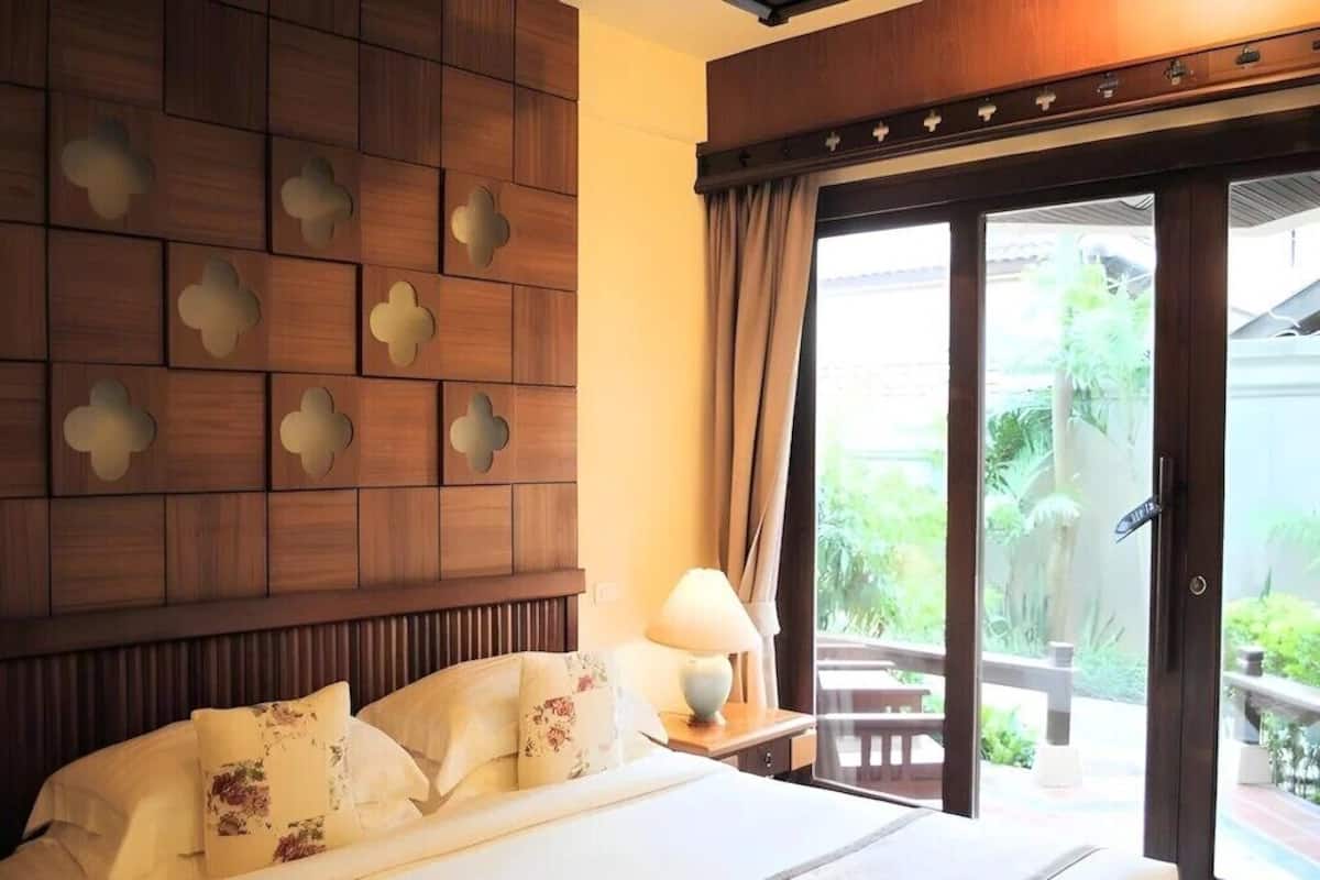 Quarto de hotel com cama, mesa de cabeceira, luminária e porta de vidro deslizante para área externa.
