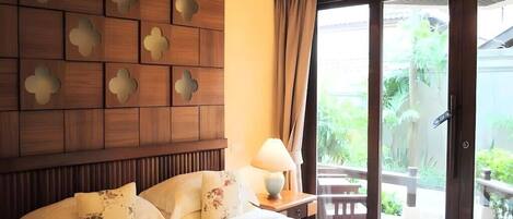 A hotel room with a bed, a nightstand, a lamp, and a sliding glass door leading to an outdoor area.