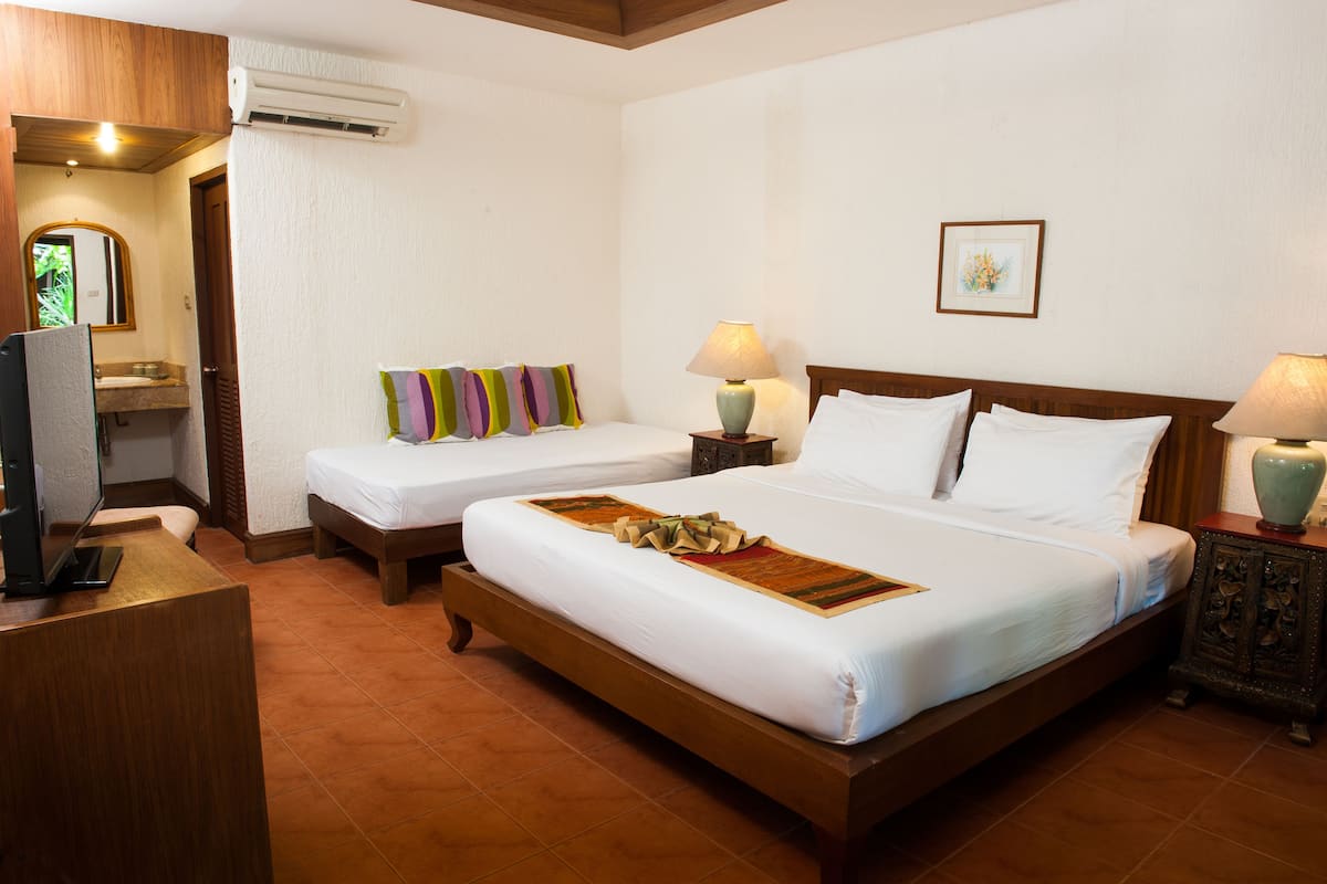 Quarto de hotel com duas camas, uma escrivaninha, televisão e banheiro visível através de uma porta aberta.