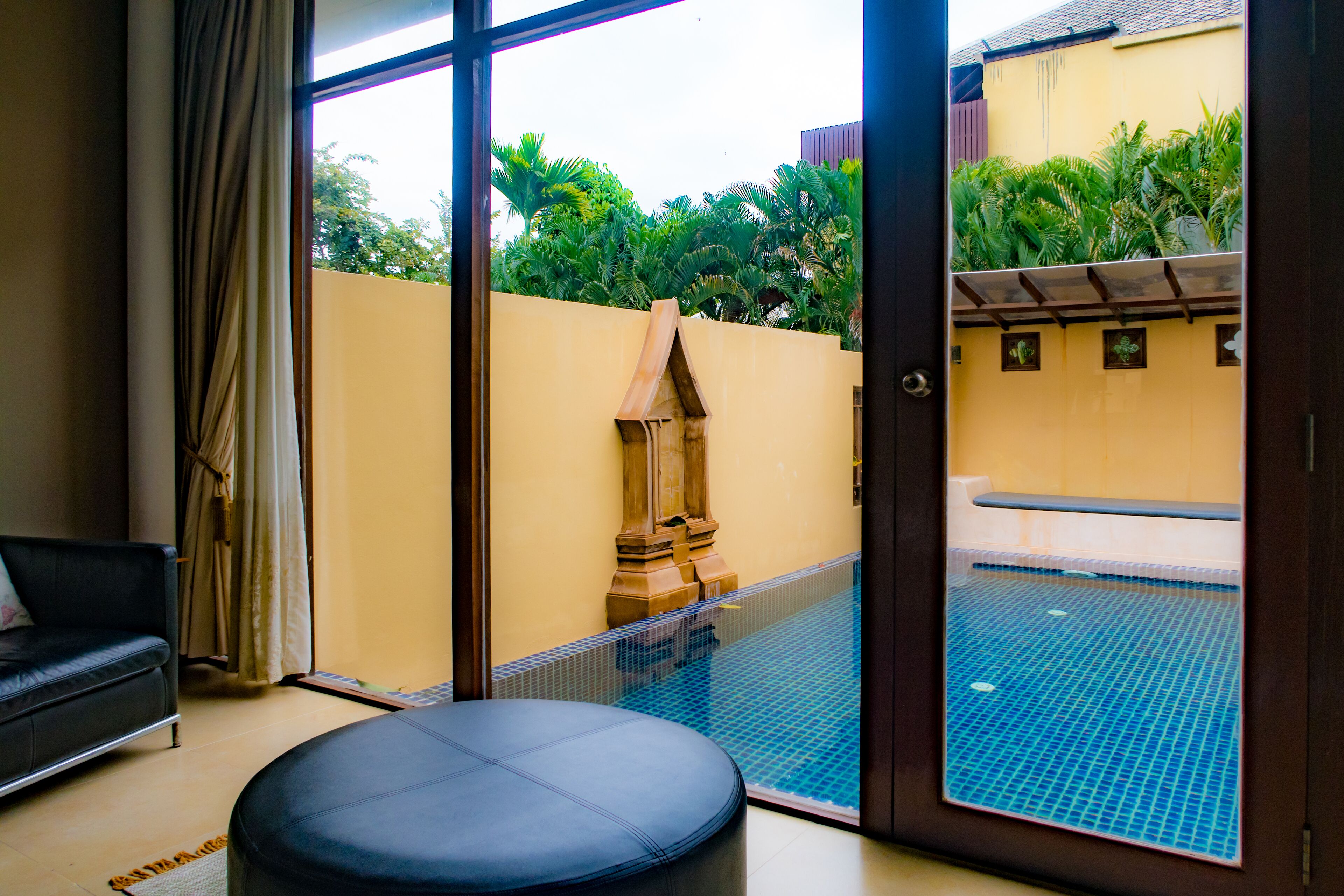 A room with a glass door leading to a swimming pool, a black leather sofa, and a tiled floor.