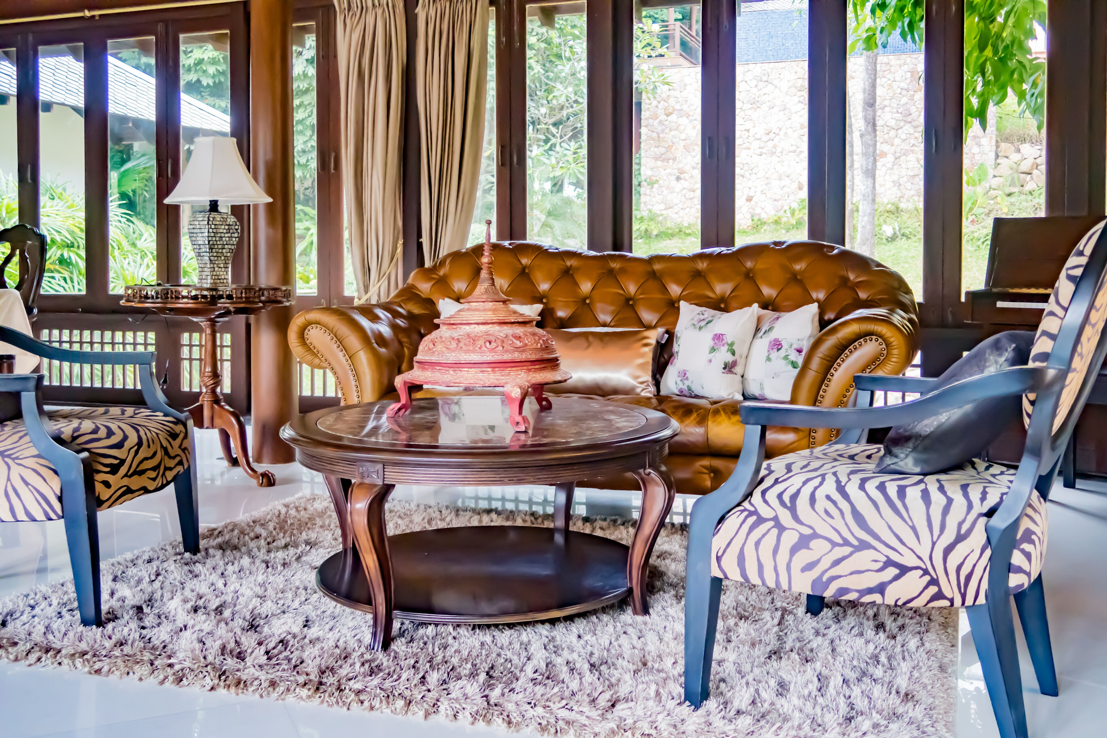A cozy seating area with a brown tufted sofa, two patterned armchairs, and a round table with a decorative item.