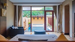 Quarto de hotel com uma grande porta de vidro deslizante para uma área de piscina, uma cama com vista, um pequeno espaço de estar e um banco de madeira.