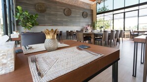 Interior de restaurante com mesa de madeira, jogos americanos de tecido e um arranjo decorativo.