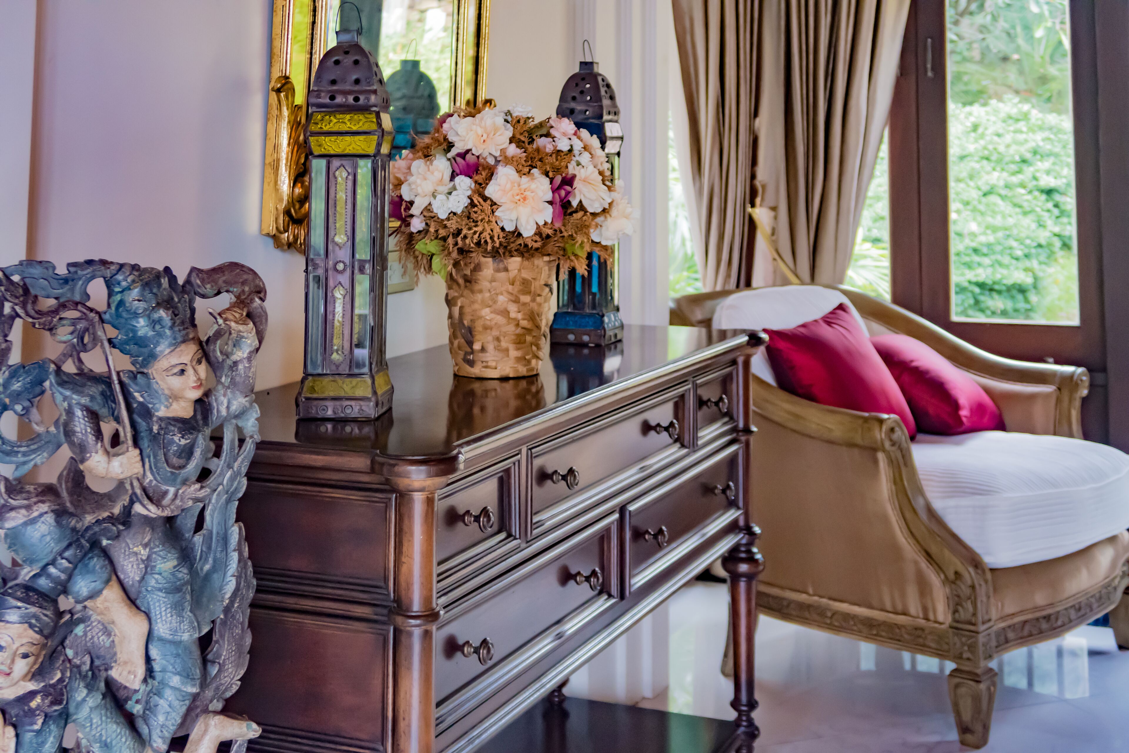 Une pièce comprenant une commode en bois, une chaise avec un coussin rouge et un vase de fleurs.