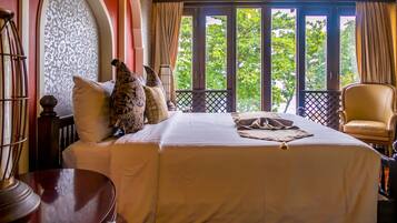 A hotel room with a large bed, a wooden chair, and a view of trees through the window.