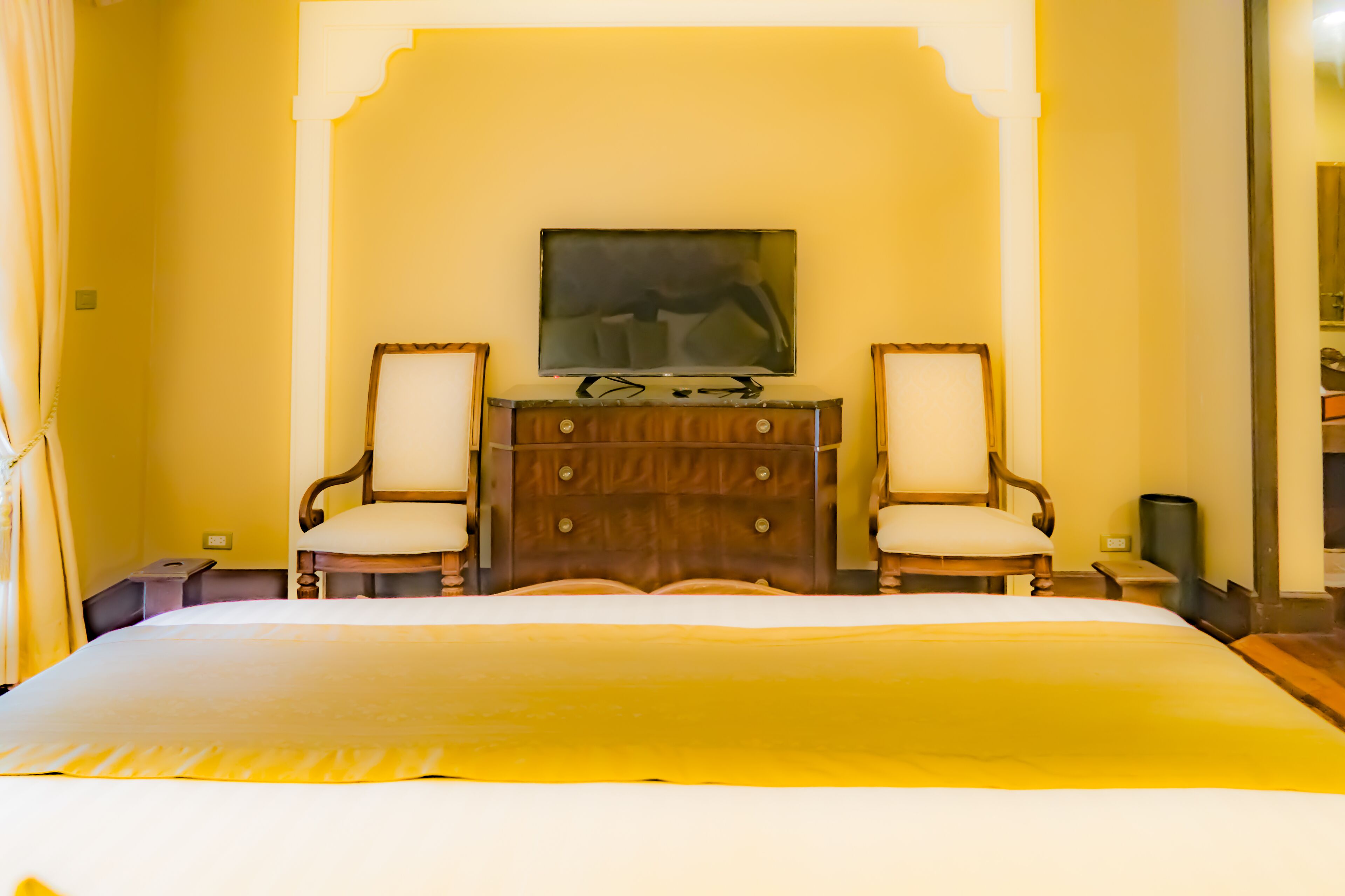 Een hotelkamer met een groot bed, twee stoelen, een dressoir en een flatscreen televisie aan de muur.