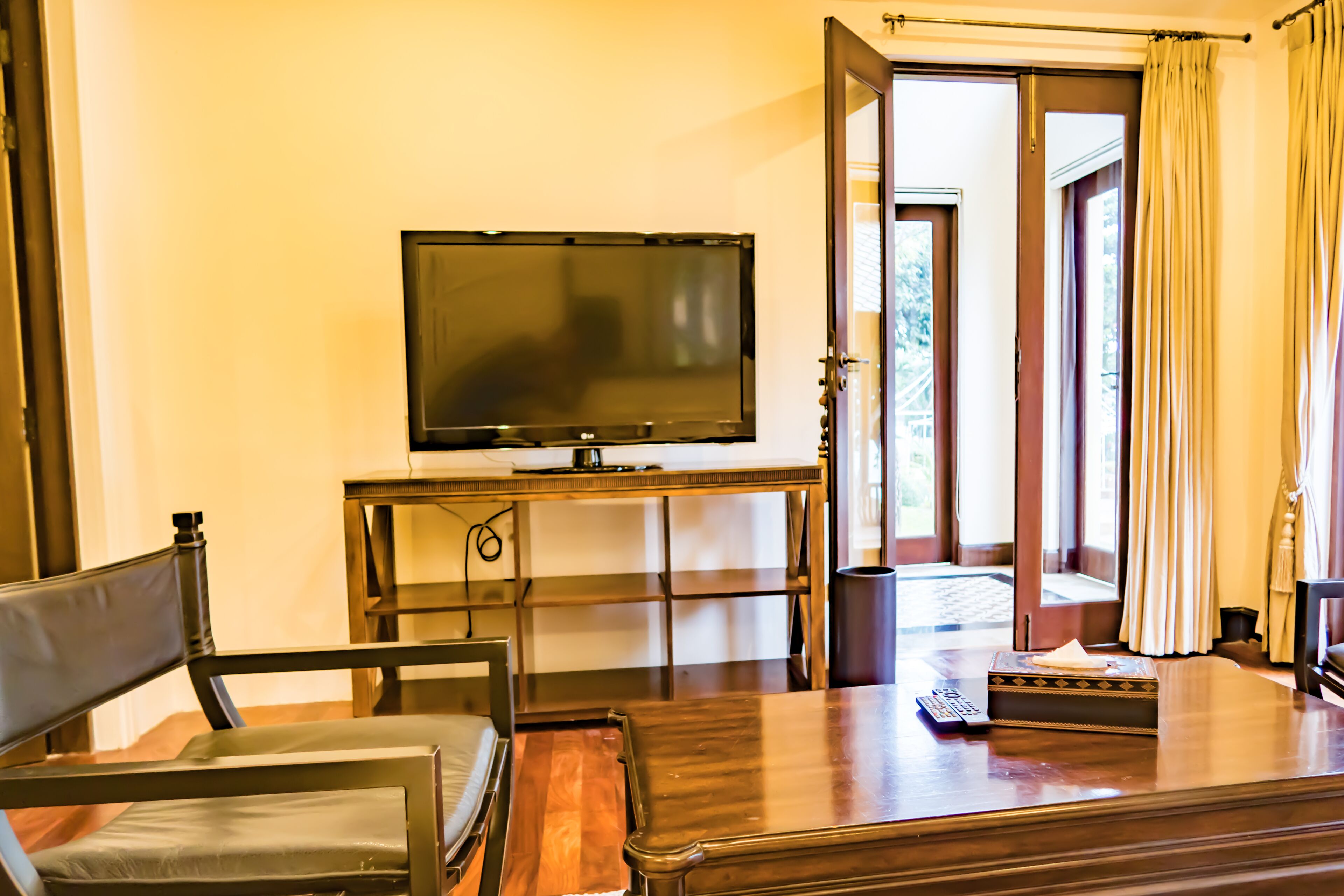 Una habitación con una televisión sobre un mueble bajo, un escritorio de madera, una silla y una puerta que da al exterior.
