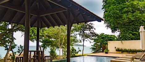 A poolside area with a pergola, lounge chairs, and a view of the sea.