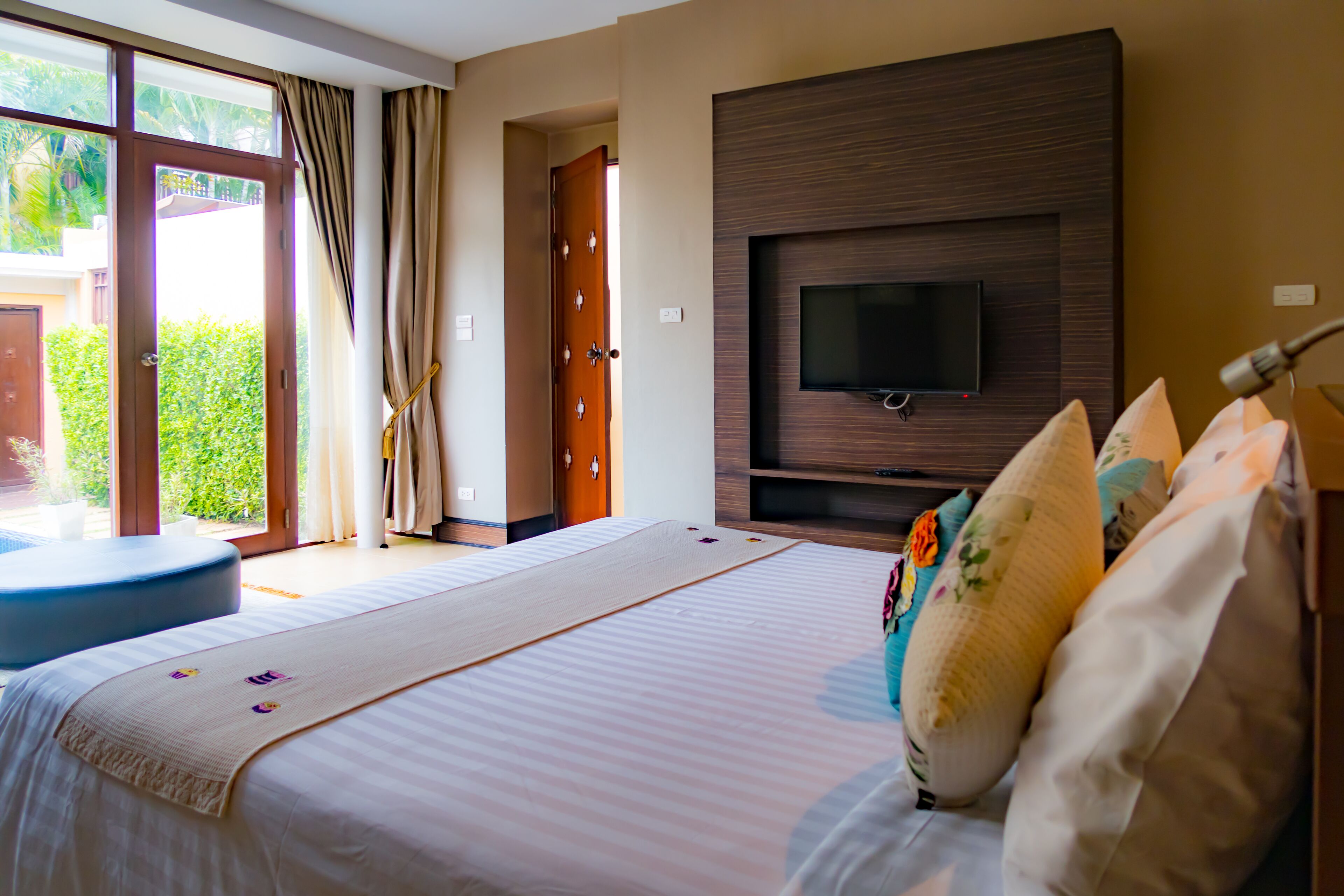 A bedroom with a large bed, a TV mounted on the wall, and a view of the outdoors.