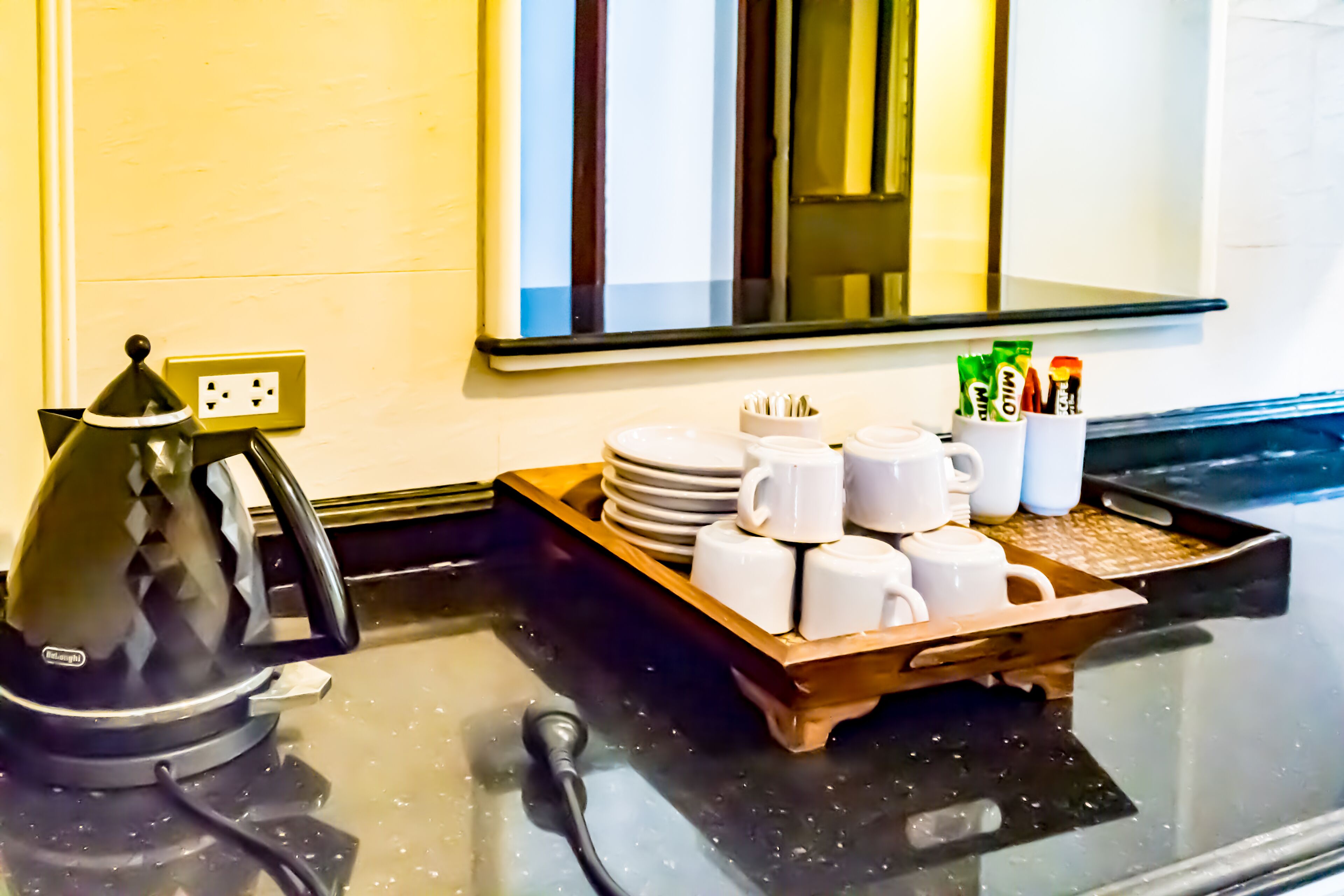 A kitchen counter with a kettle, a tray of white mugs, and a coffee machine.