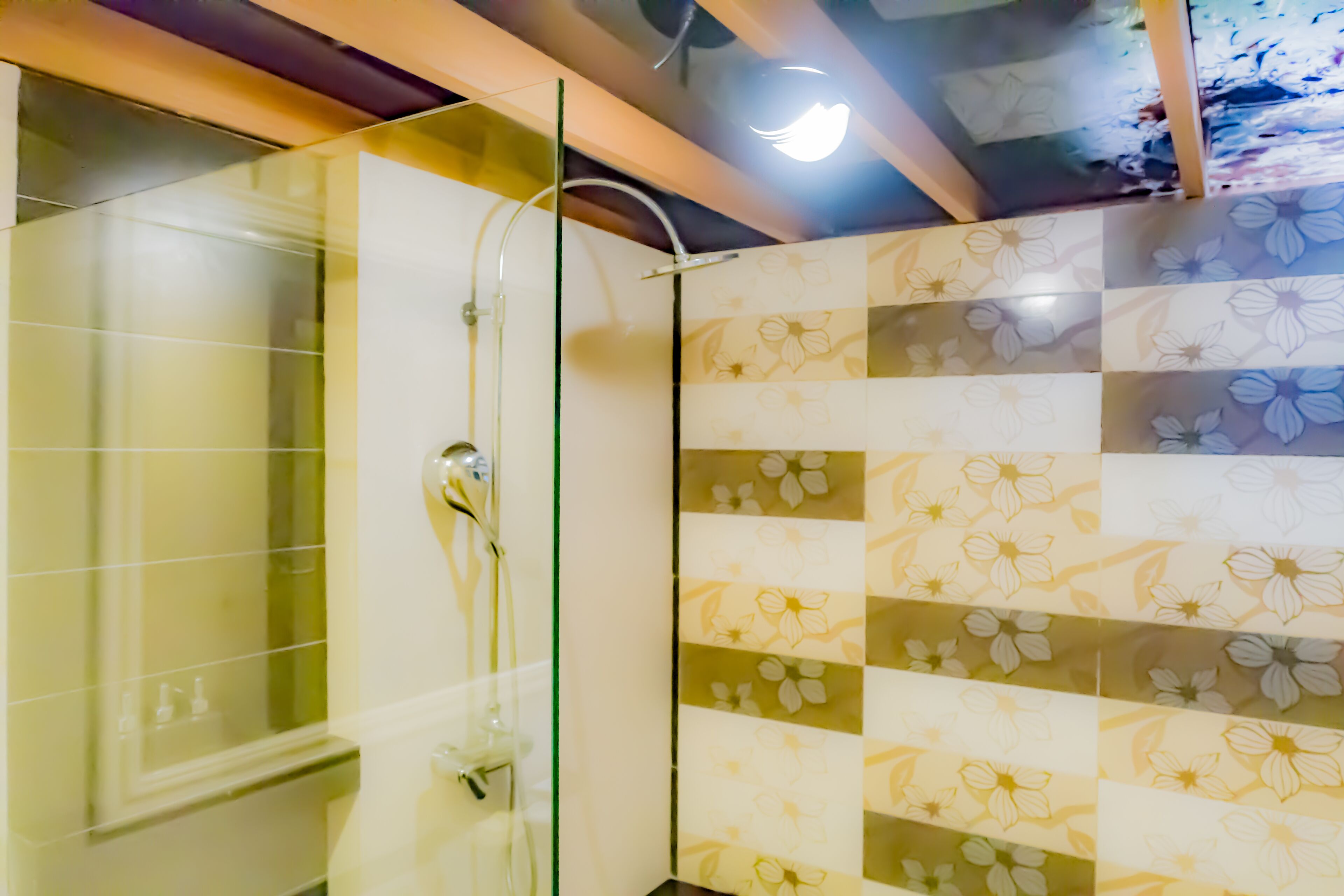 A shower area with glass doors and a tiled wall with a floral pattern.