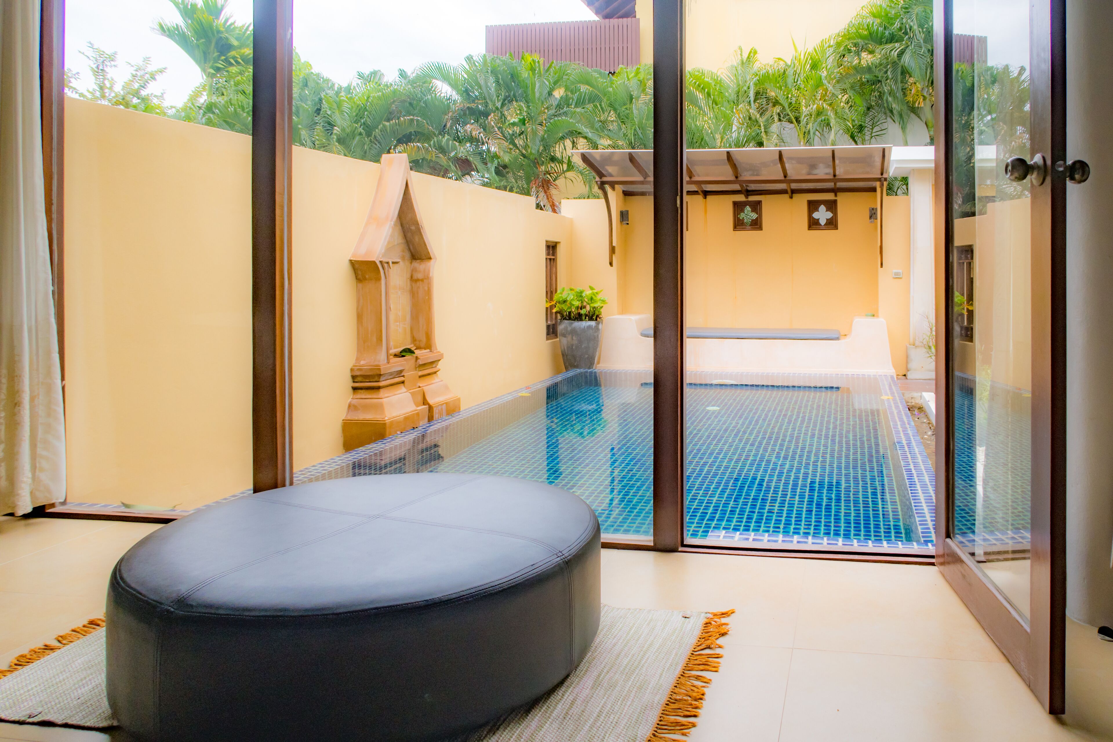 A modern room with a glass door leading to a pool area, a cushioned seating area, and a potted plant.