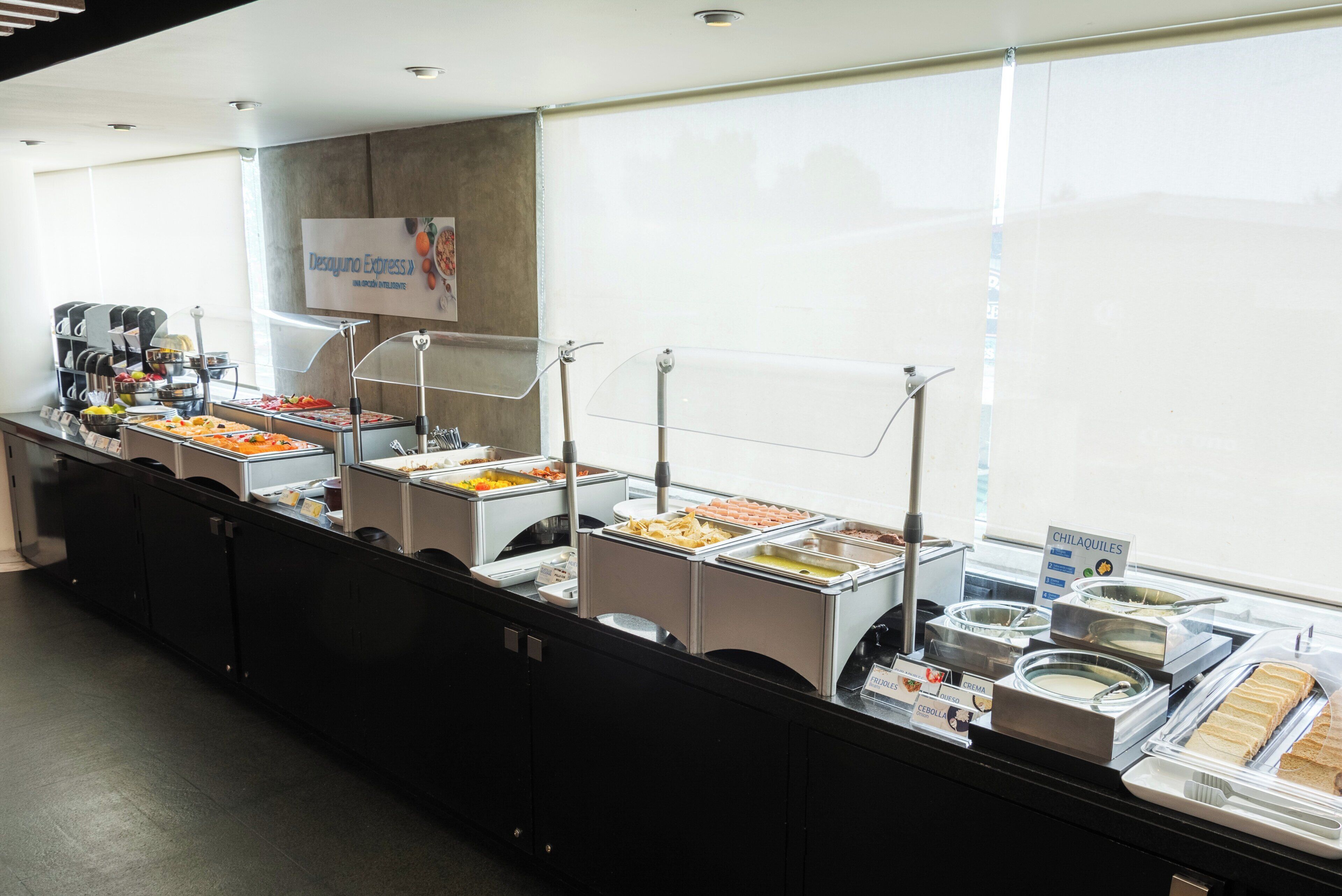 A buffet setup with various food stations, including a sign for 'Desayuno Express' and a 'CHILAQUILES' section.