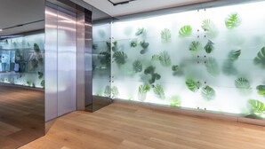 Un intérieur moderne avec une cloison en verre ornée d’un motif de feuilles, un plancher en bois et une colonne métallique.