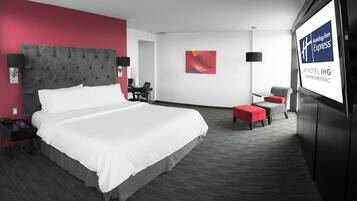 Ett hotellrum med en stor säng, ett skrivbord, en stol och en tv-skärm som visar hotellets namn.