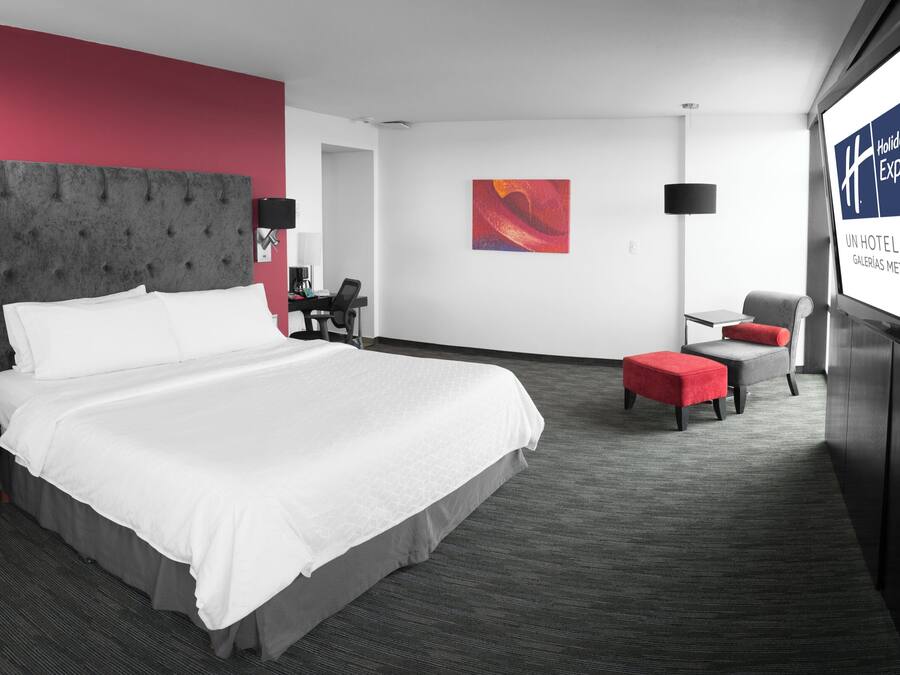 Ett hotellrum med en stor säng, ett skrivbord, en stol och en tv-skärm som visar hotellets namn.