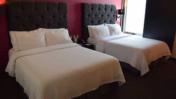 Quarto de hotel com duas camas, cada uma com cabeceira escura e roupa de cama branca.