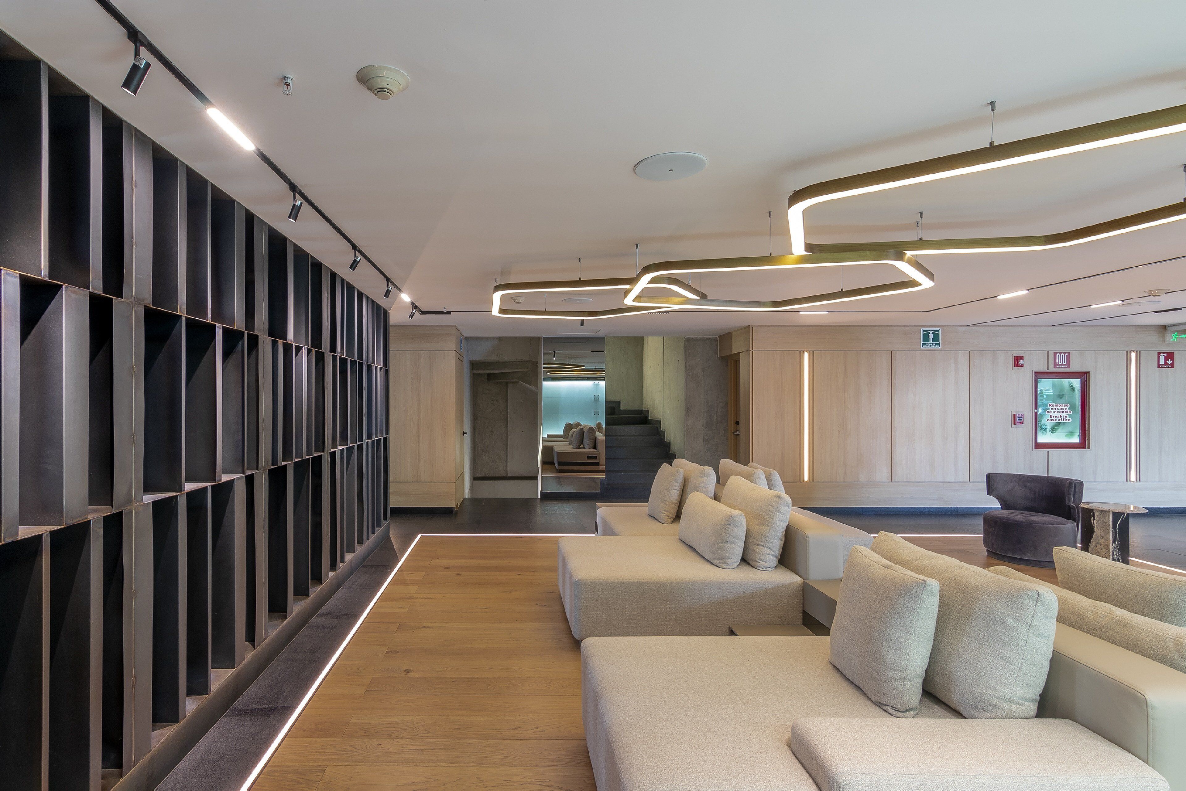 A modern lobby with a long reception desk, seating area with sofas, and a staircase leading to upper floors.