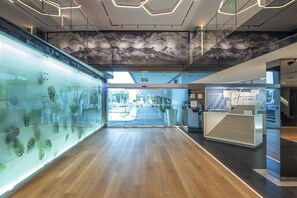 A modern hotel lobby with a wooden floor, a reception desk, and a glass wall displaying plant images. - Holiday Inn Express Toluca Galerias Metepec by IHG (Toluca)