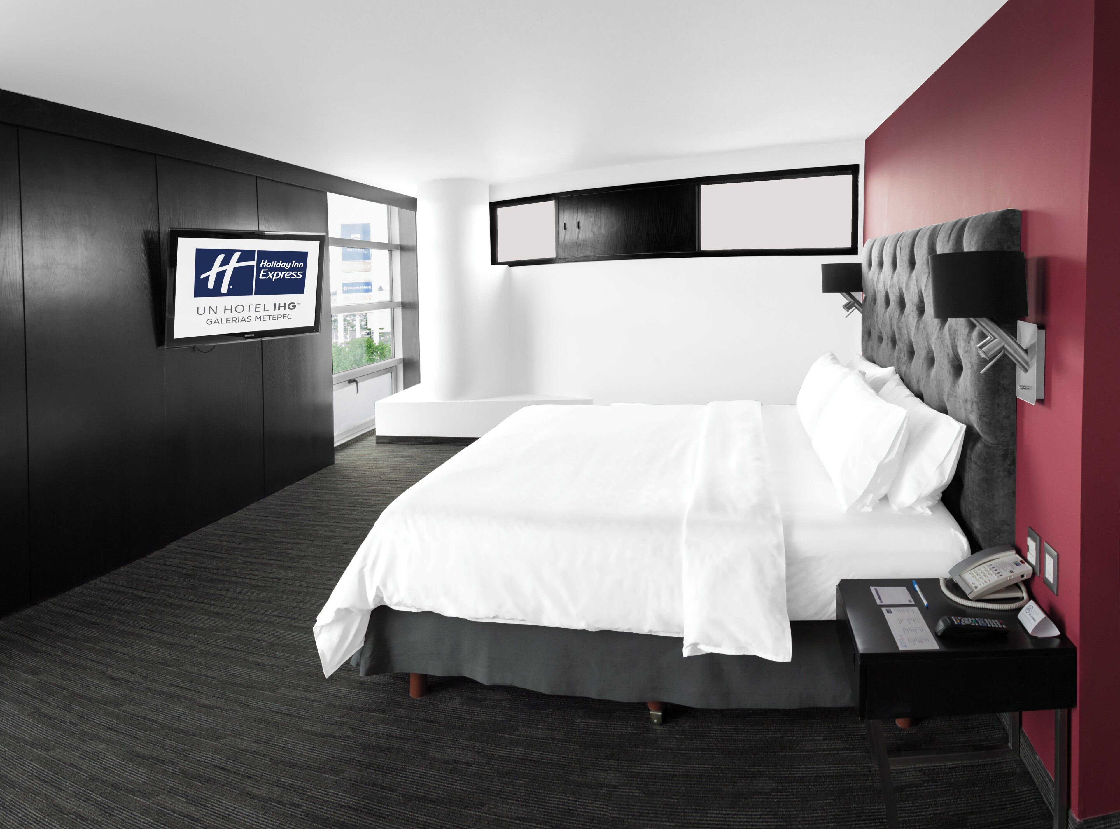 A modern hotel room with a large bed, a nightstand, a television, and a window with a view.
