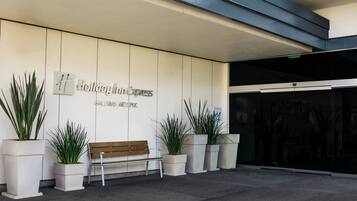 Entrada de hotel con un banco, plantas en macetas y un cartel que dice 'Holiday Inn Express'.