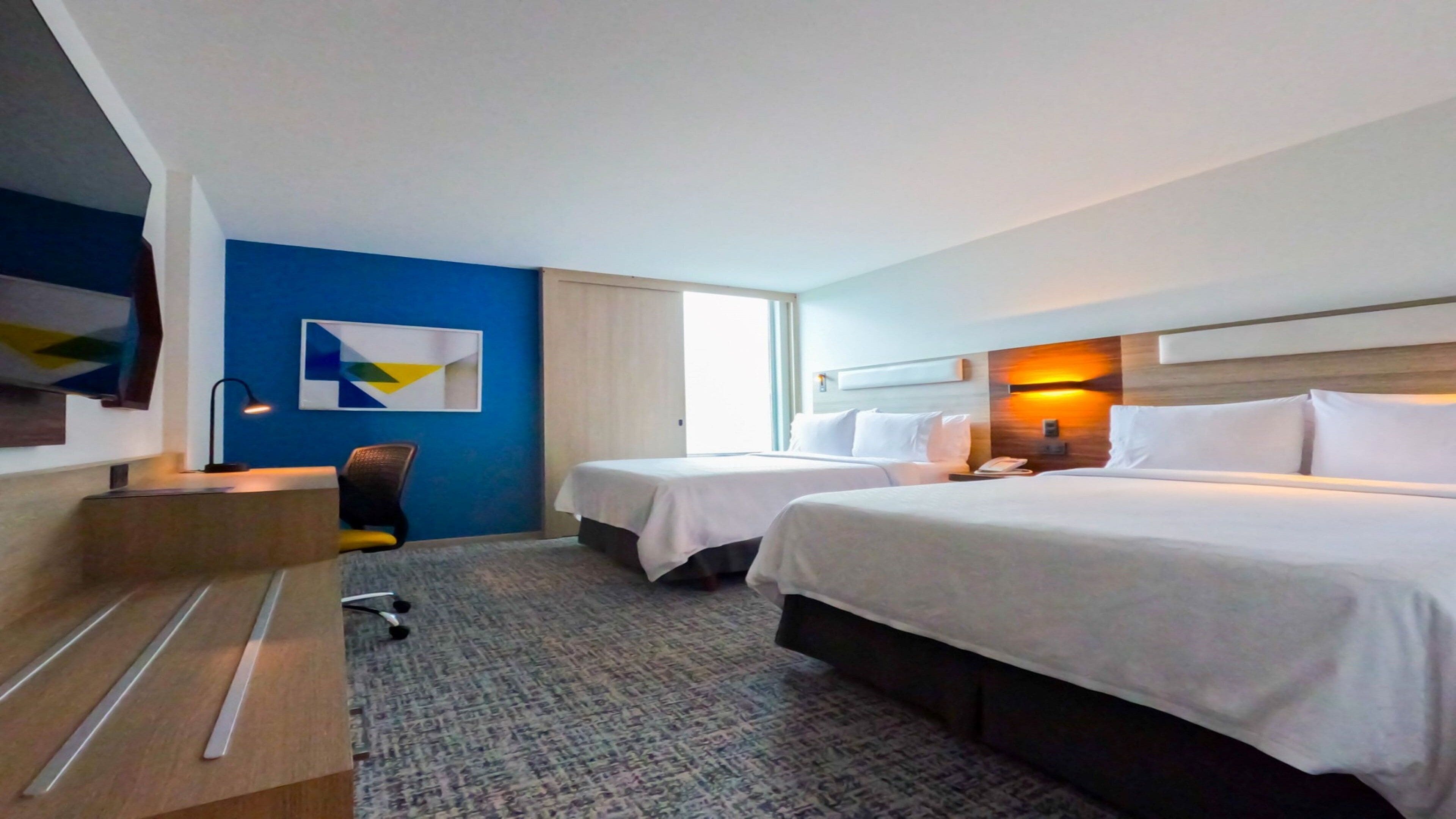 Habitación de hotel con dos camas, un escritorio, una silla y un ventanal grande.
