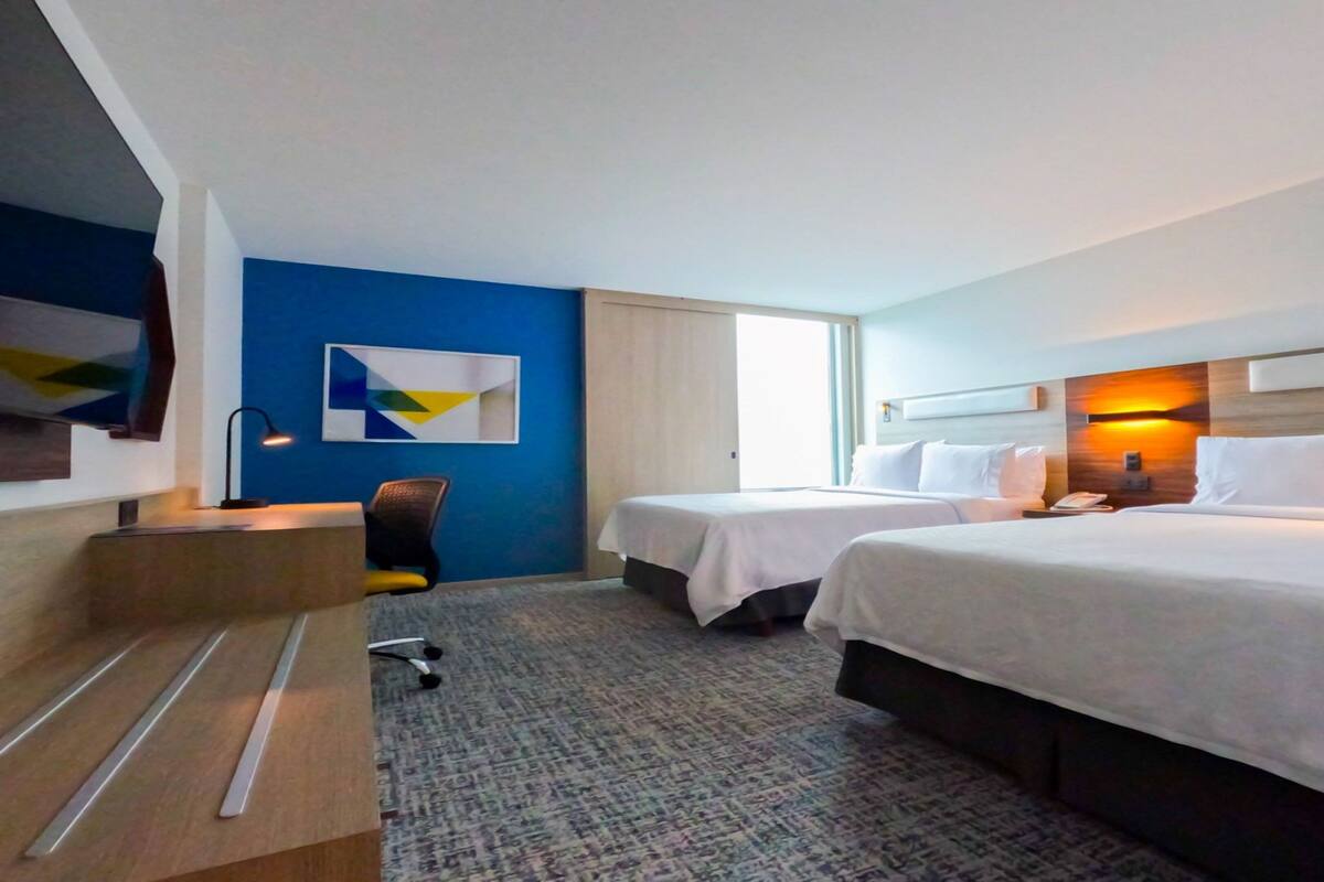 A hotel room with two beds, a desk, a chair, and a large window.