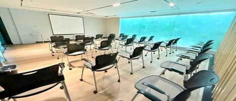 A conference room with rows of chairs, a projector screen, and a large window with a view of a pool.