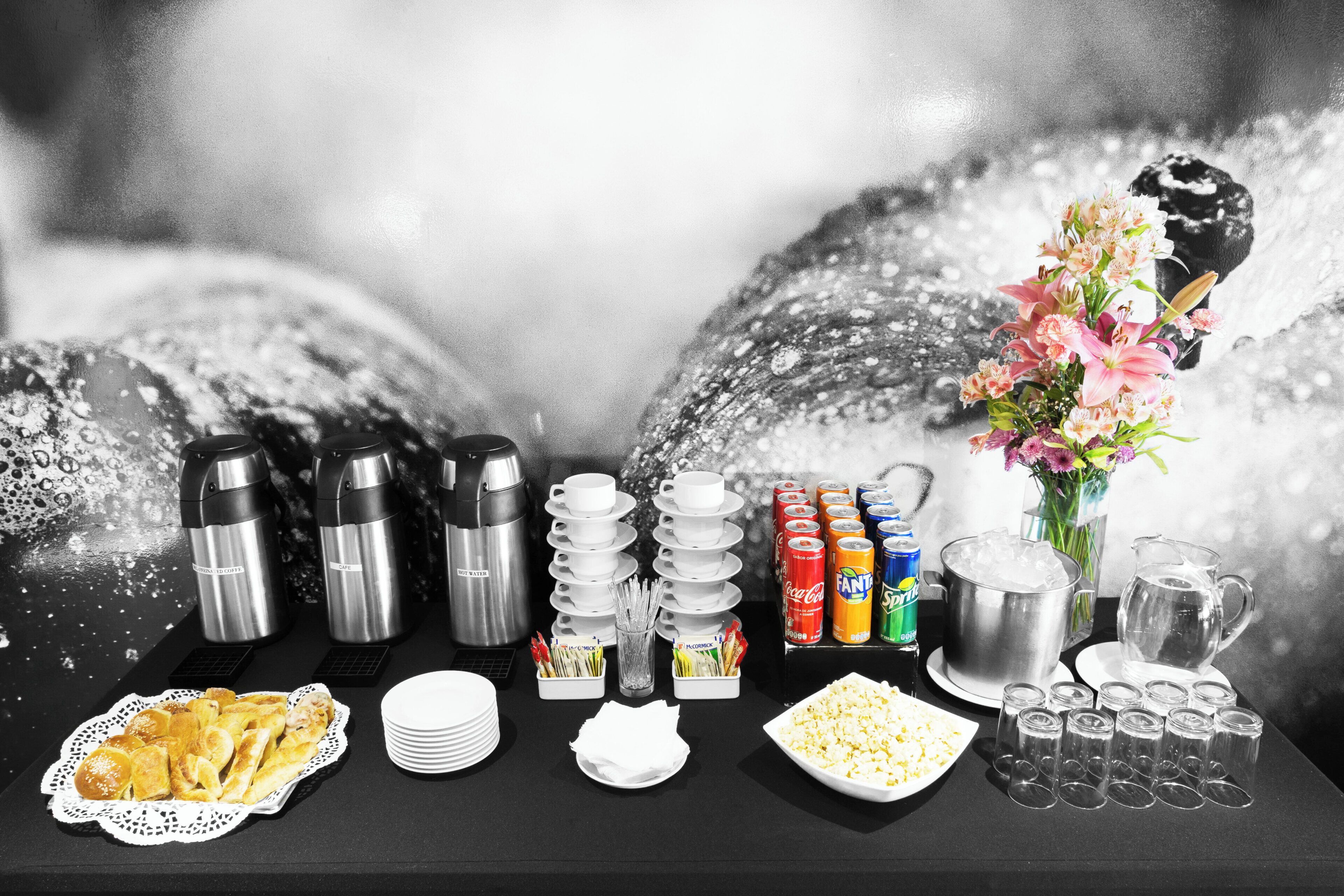 A breakfast buffet setup with coffee makers, hot water, plates, cups, and various beverages.