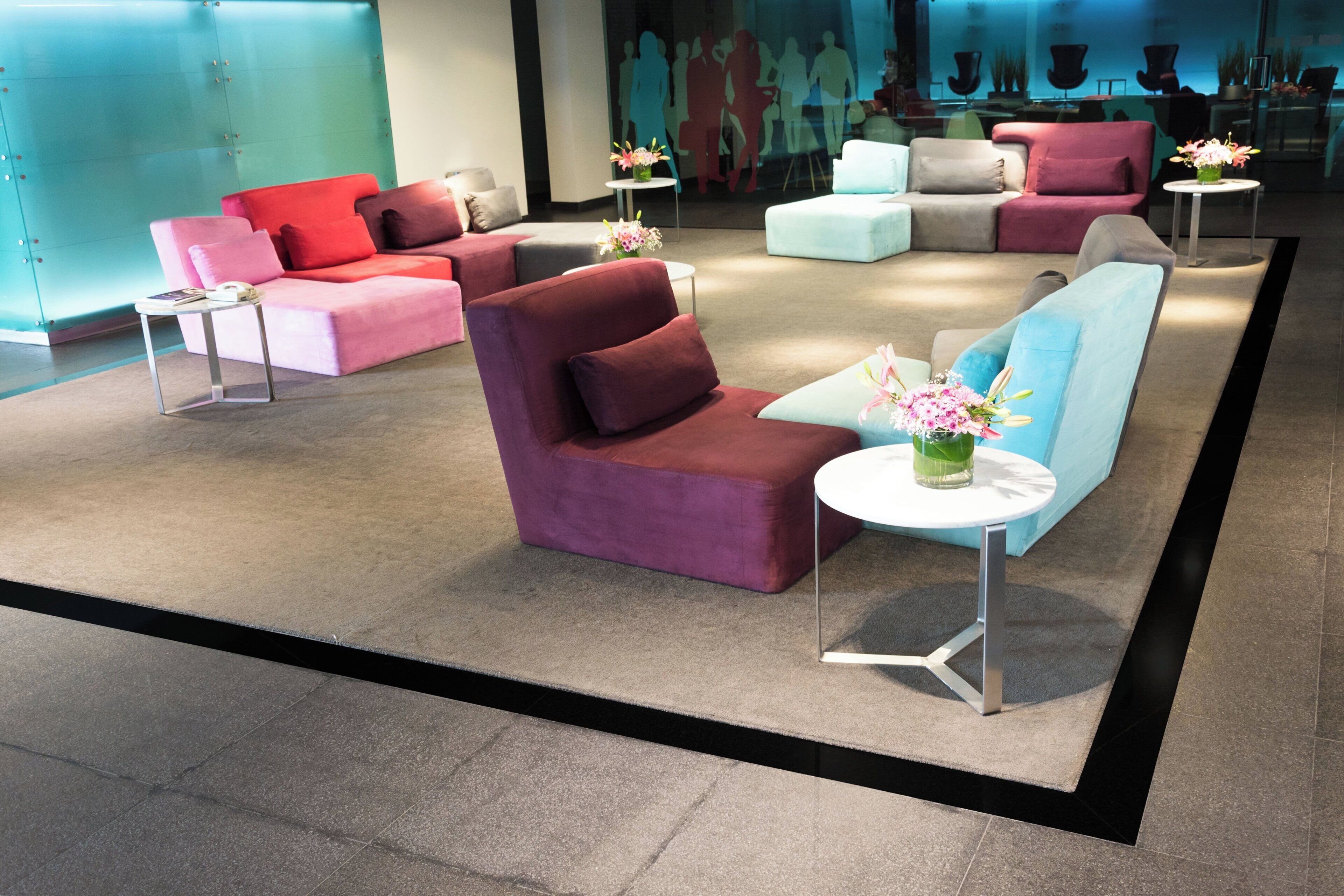 A modern lounge area with sofas and armchairs arranged around small tables, some with floral centerpieces.