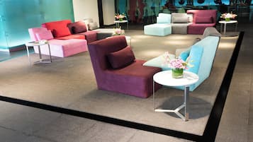 A modern lounge area with sofas and armchairs arranged around small tables, some with floral centerpieces.