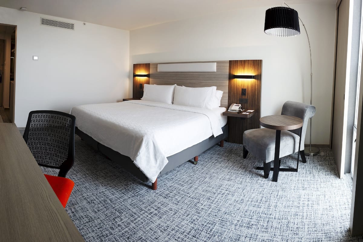 Habitación de hotel con una cama grande, un escritorio, una silla y una mesita de noche con lámpara.