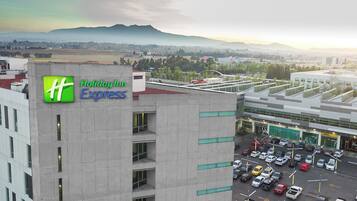 Edificio de Holiday Inn Express con vista a un estacionamiento y montañas a la distancia.