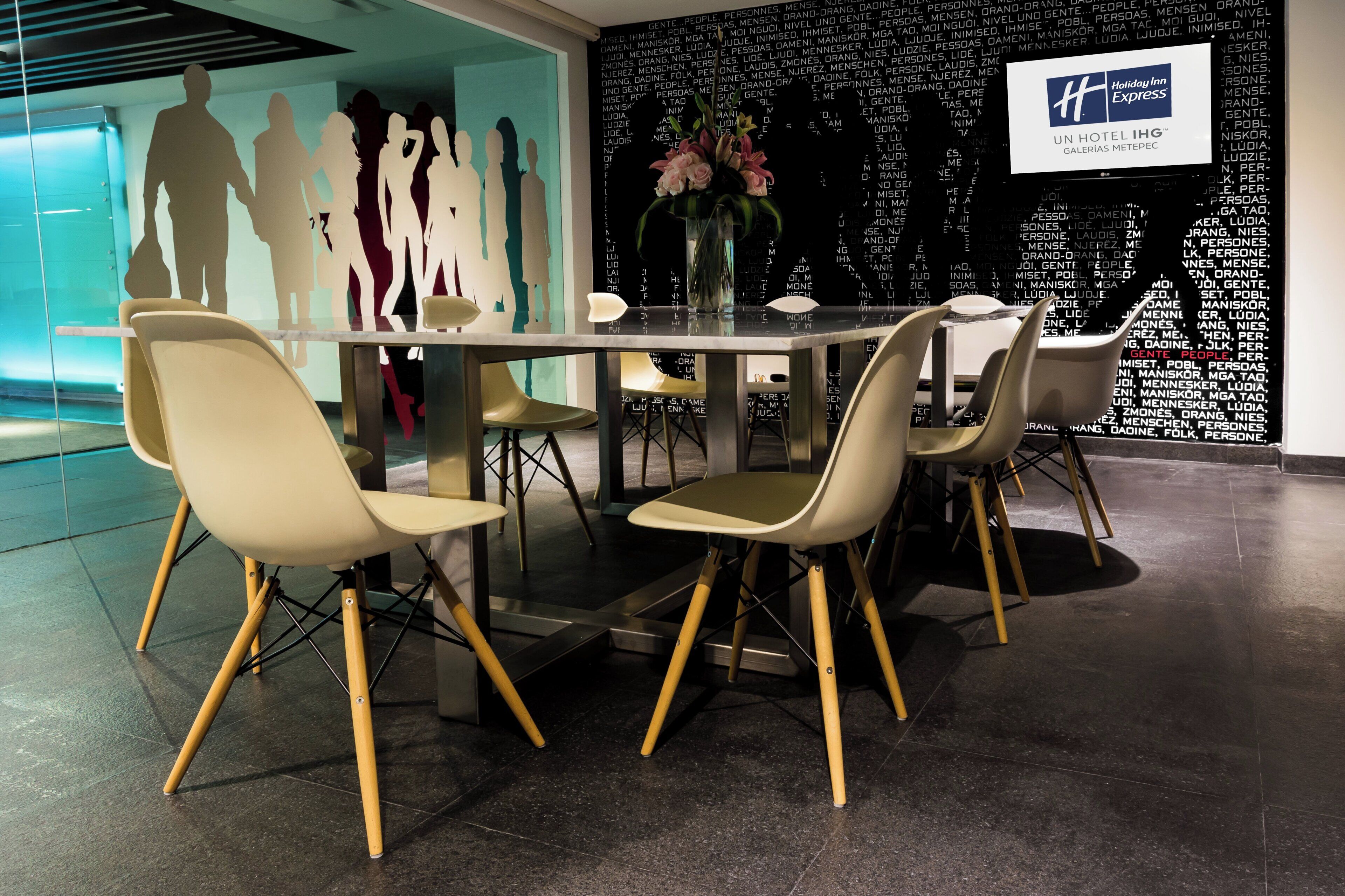 Un hall d’hôtel moderne avec une table en verre entourée de chaises, un mur décoratif orné de silhouettes et un panneau indiquant « Holiday Inn Express ».