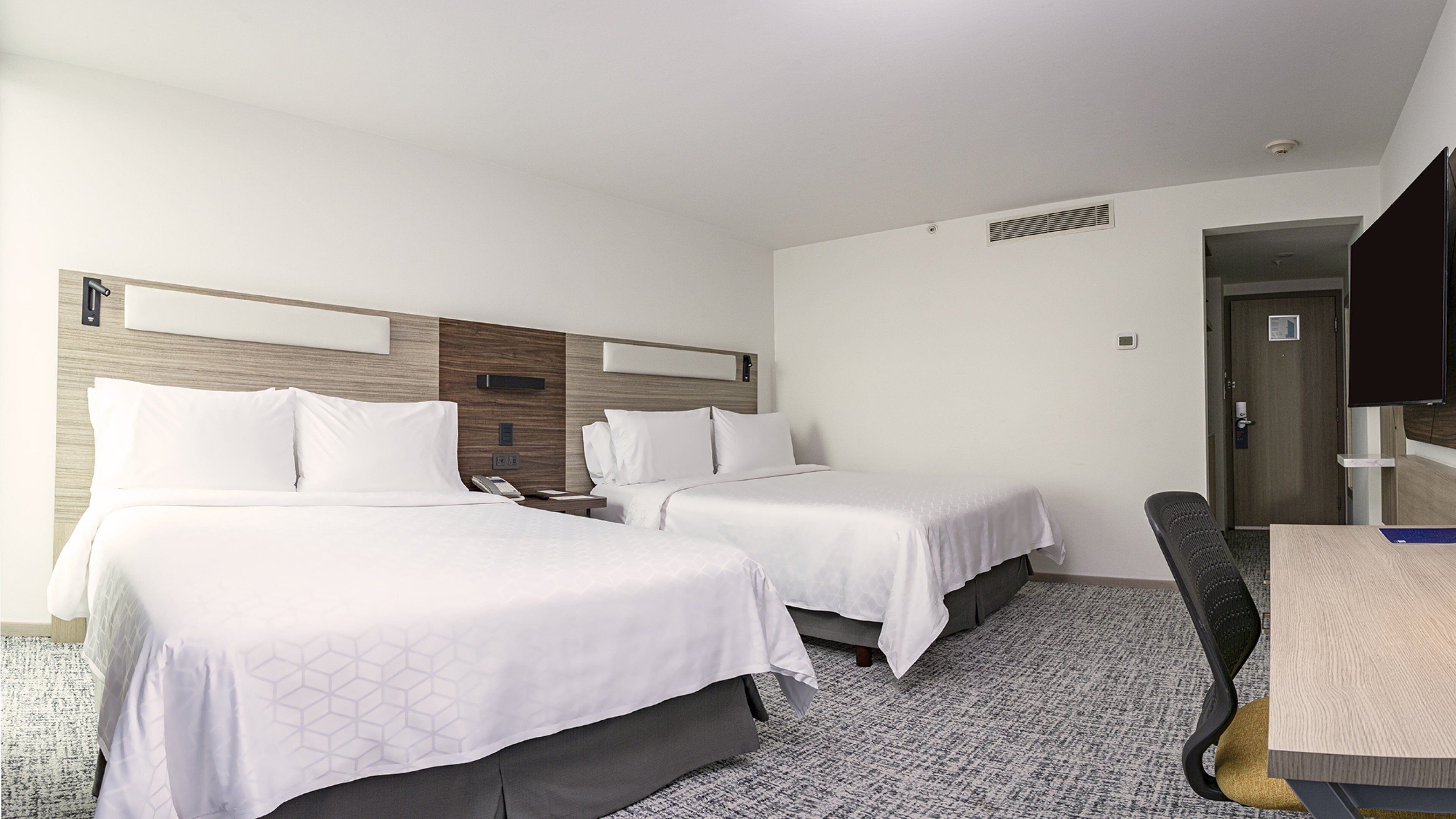 A hotel room with two beds, a desk, a chair, and a television.