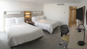 Habitación de hotel con dos camas, un escritorio, una silla, un televisor y una lámpara fijada a la pared.