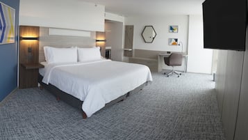 A hotel room with a large bed, a desk, a chair, and a TV.
