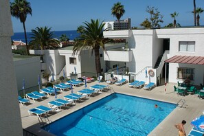 A pool area with lounge chairs, a swimming pool, and a view of the ocean. - El Sombrero Apartments Los Gigantes (Santiago del Teide)
